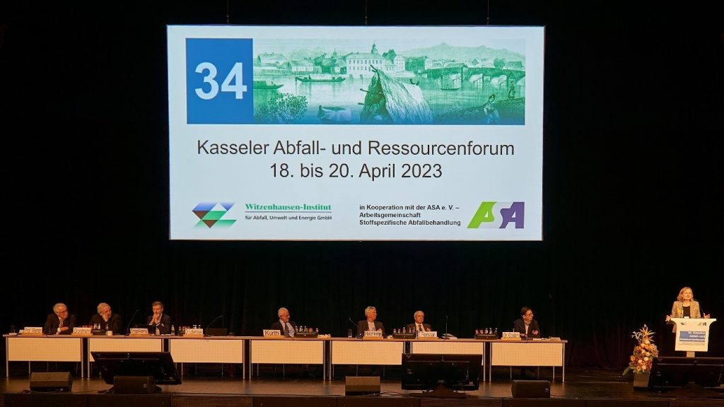 Blick auf das Podium mit sieben Experten und einer Expertin am Rednerpult, im Hintergrund eine Projektion: Kasseler Abfall- und Ressourcenforum 18. bis 20. April 2023
